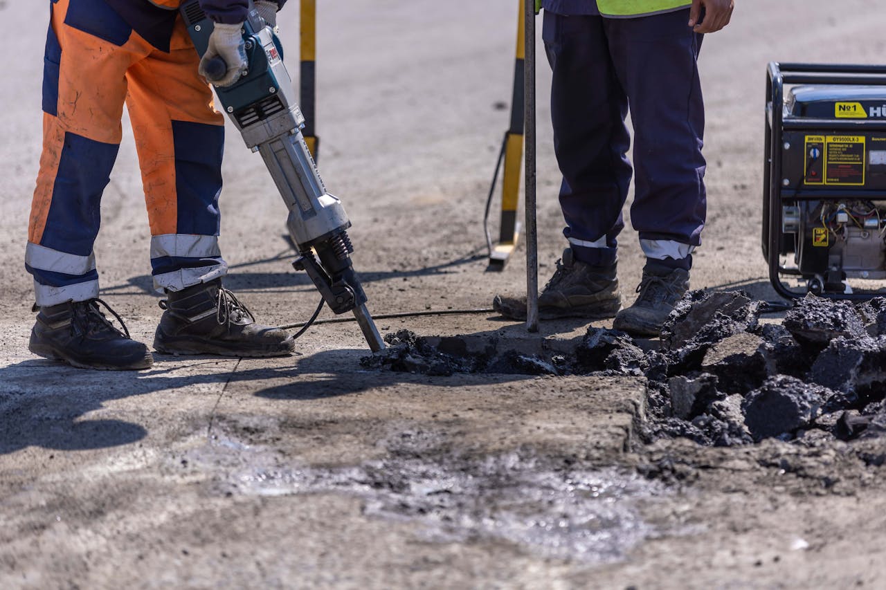 Construction workers breaking asphalt with jackhammer during road work.
