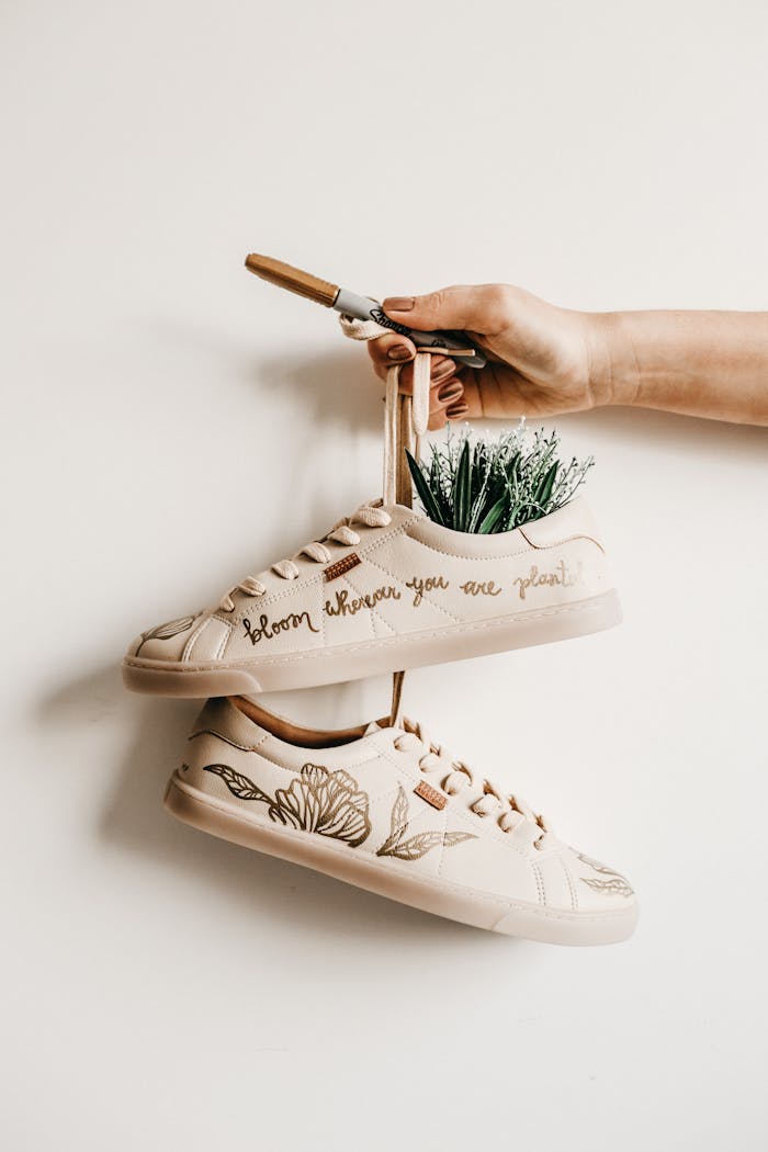 Hand holding decorated shoes with plant embroidery and creative quote design.